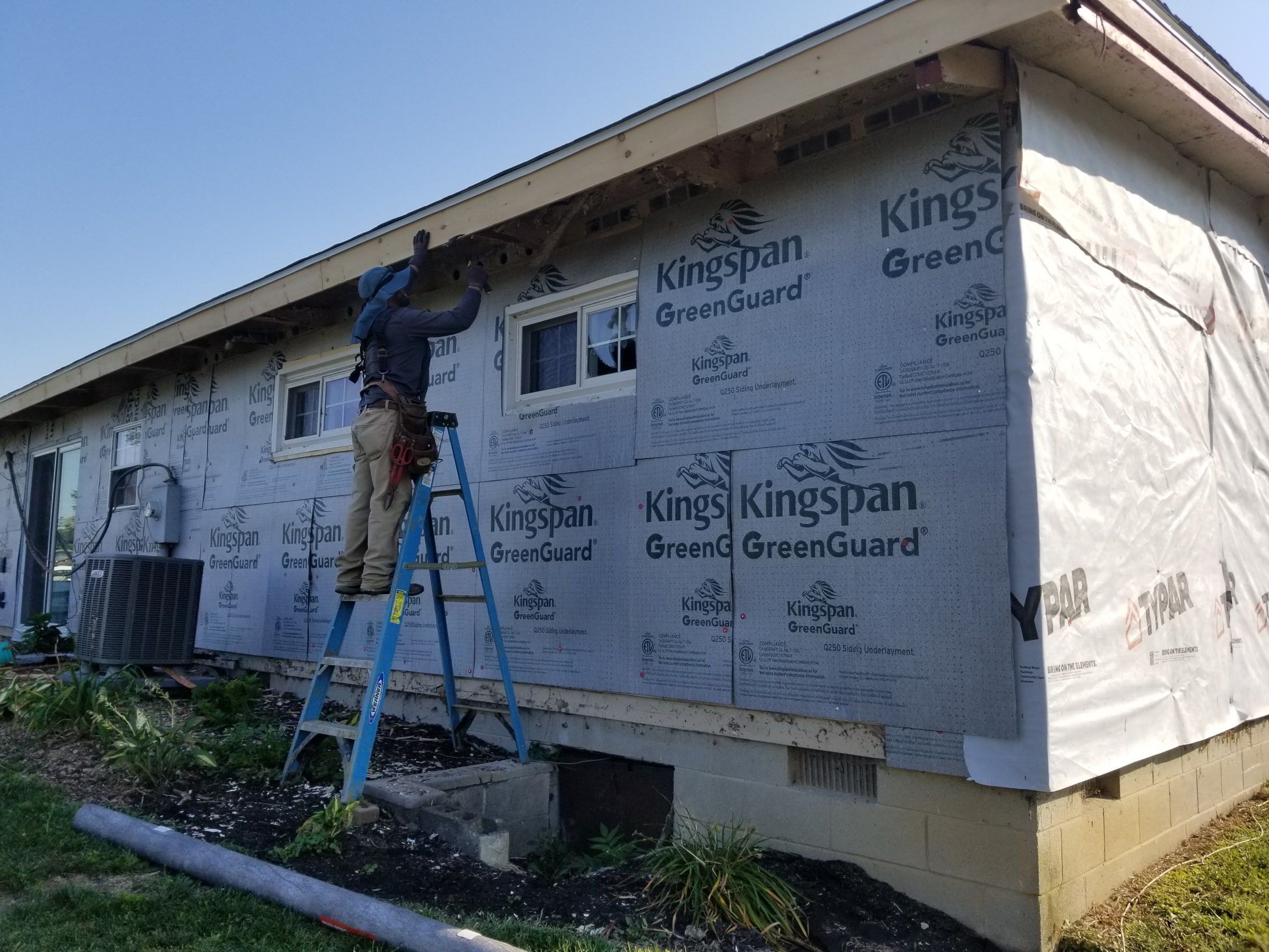 House wrap over the fanfold at the corner, with a crew member on a ladder, Beavercreek, Ohio.