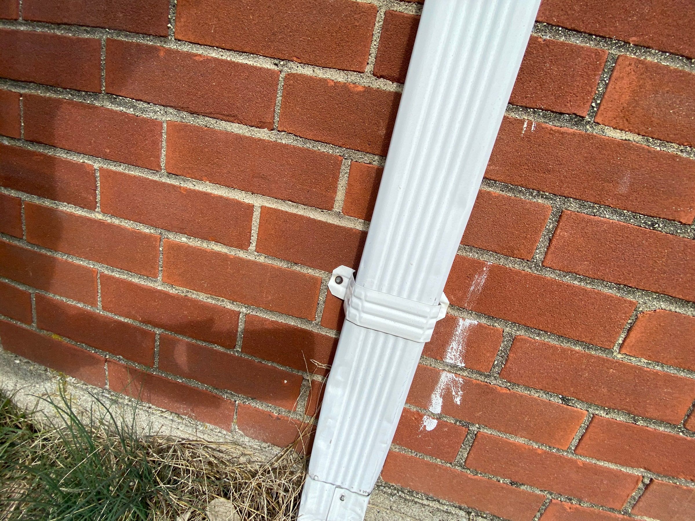 A dented white downspout against the brick wall, Kettering, Ohio.