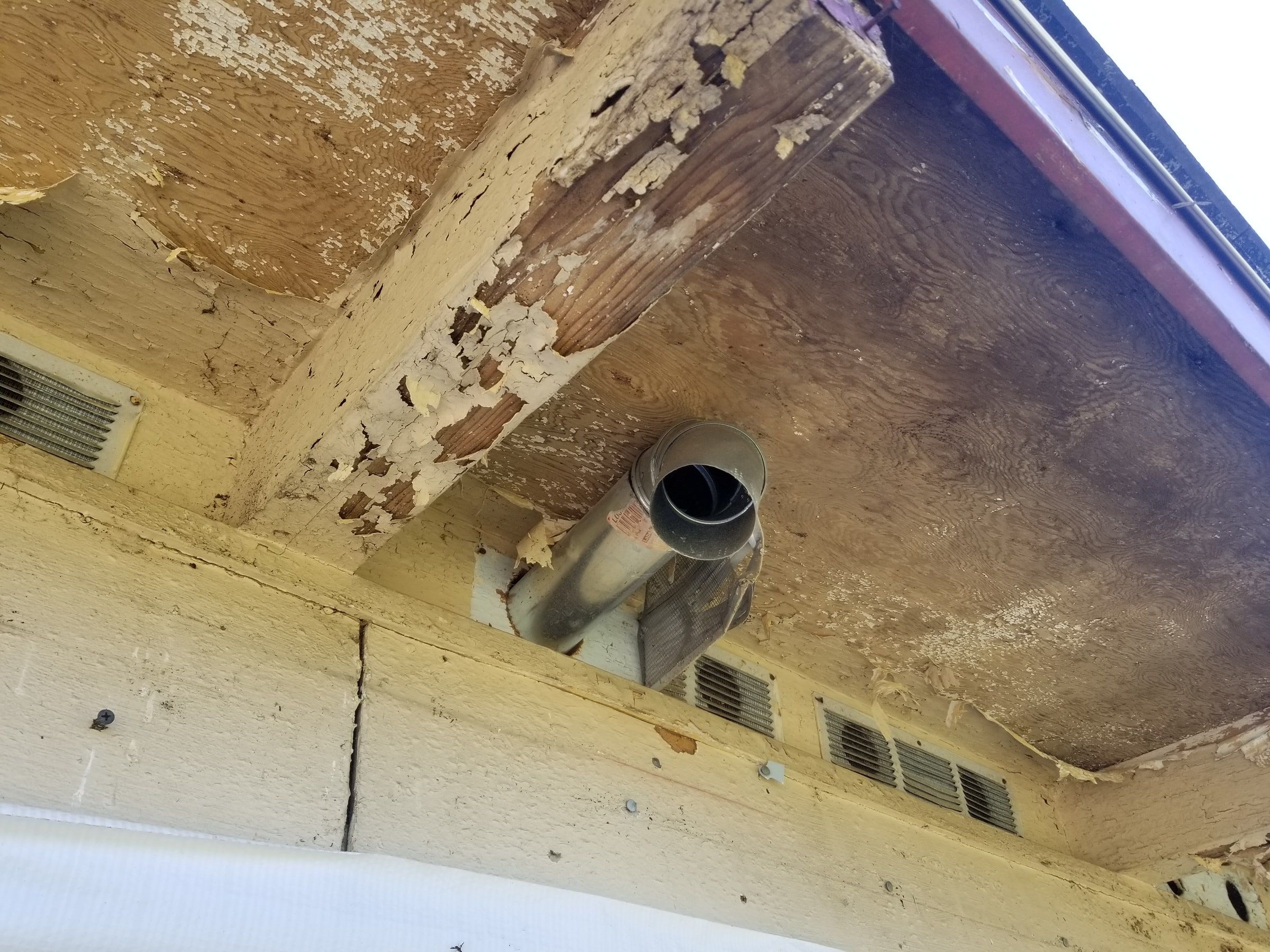 Peeling paint and worn wood at the eave above a vent, Beavercreek, Ohio.