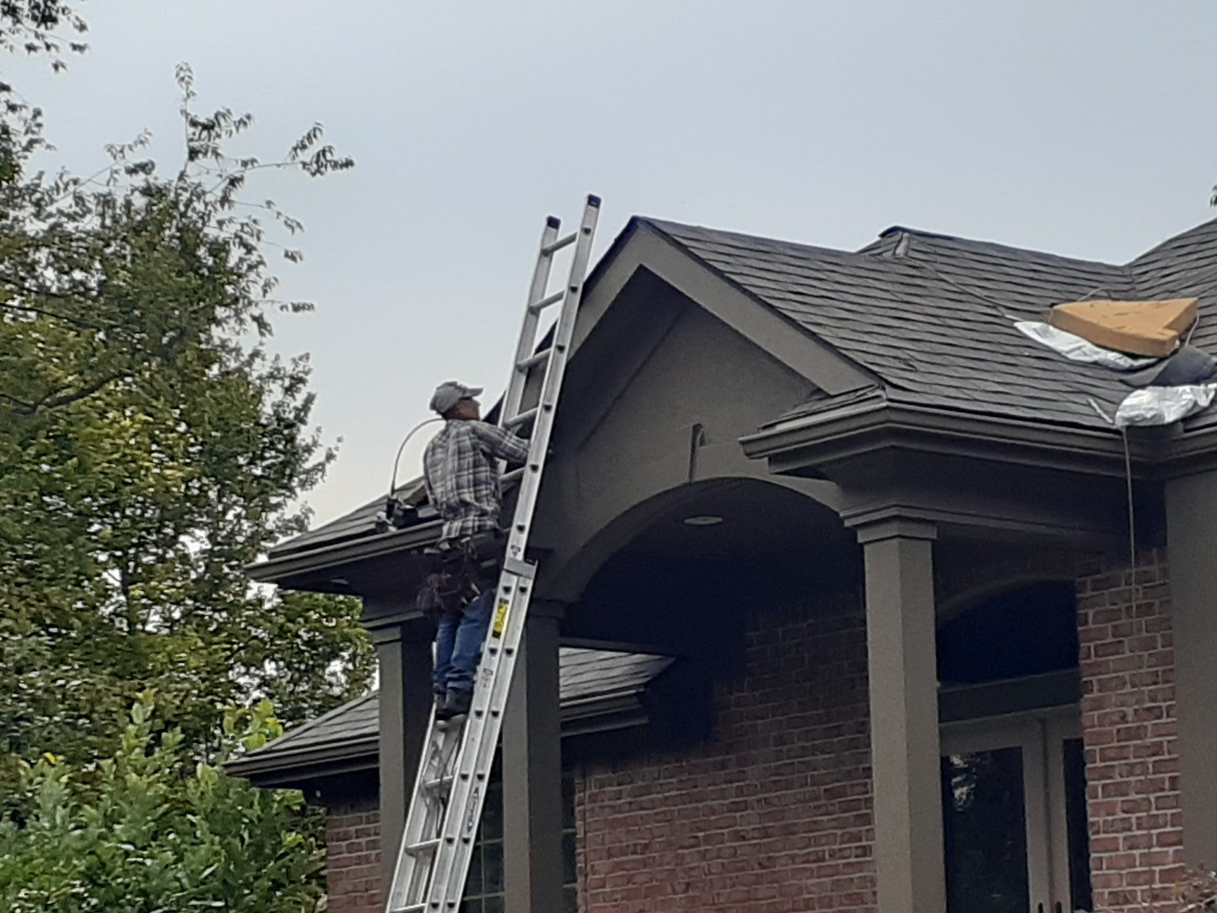 Roofer on an extension ladder at the portico