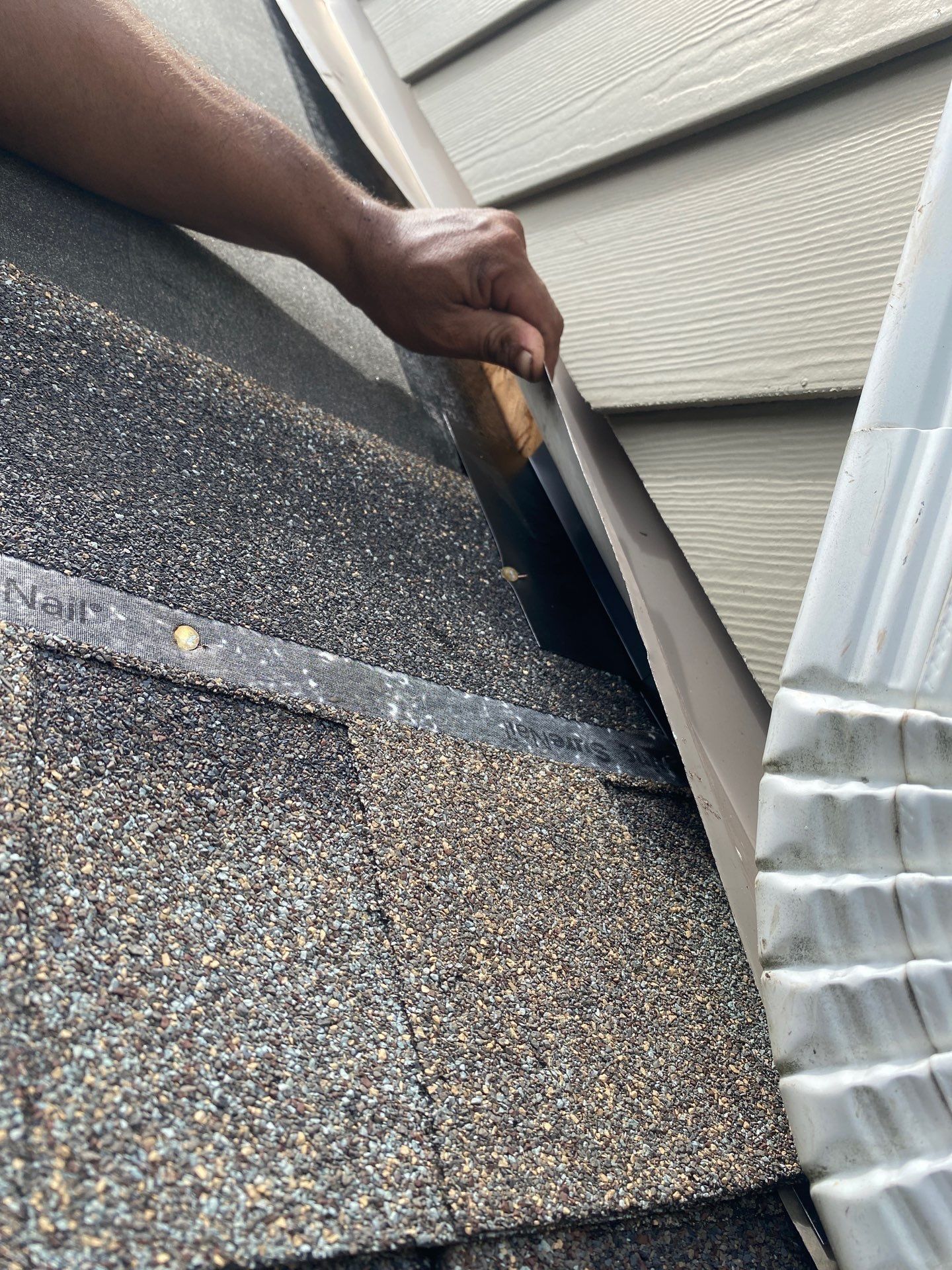 Hand lifting the siding to show flashing along the wall beside new shingles, Yellow Springs, Ohio.