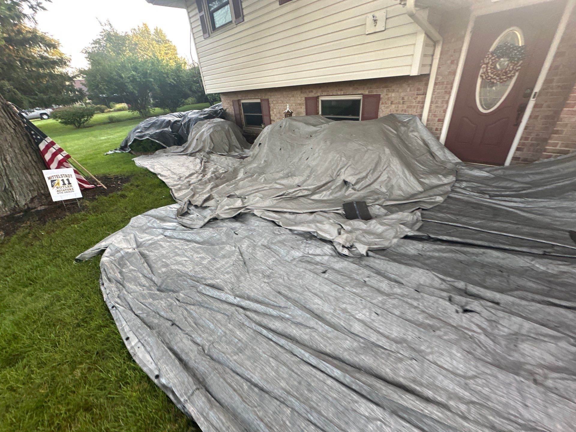 Tarps over the flower bed by the front door, with a flag in the yard, Dayton, Ohio.