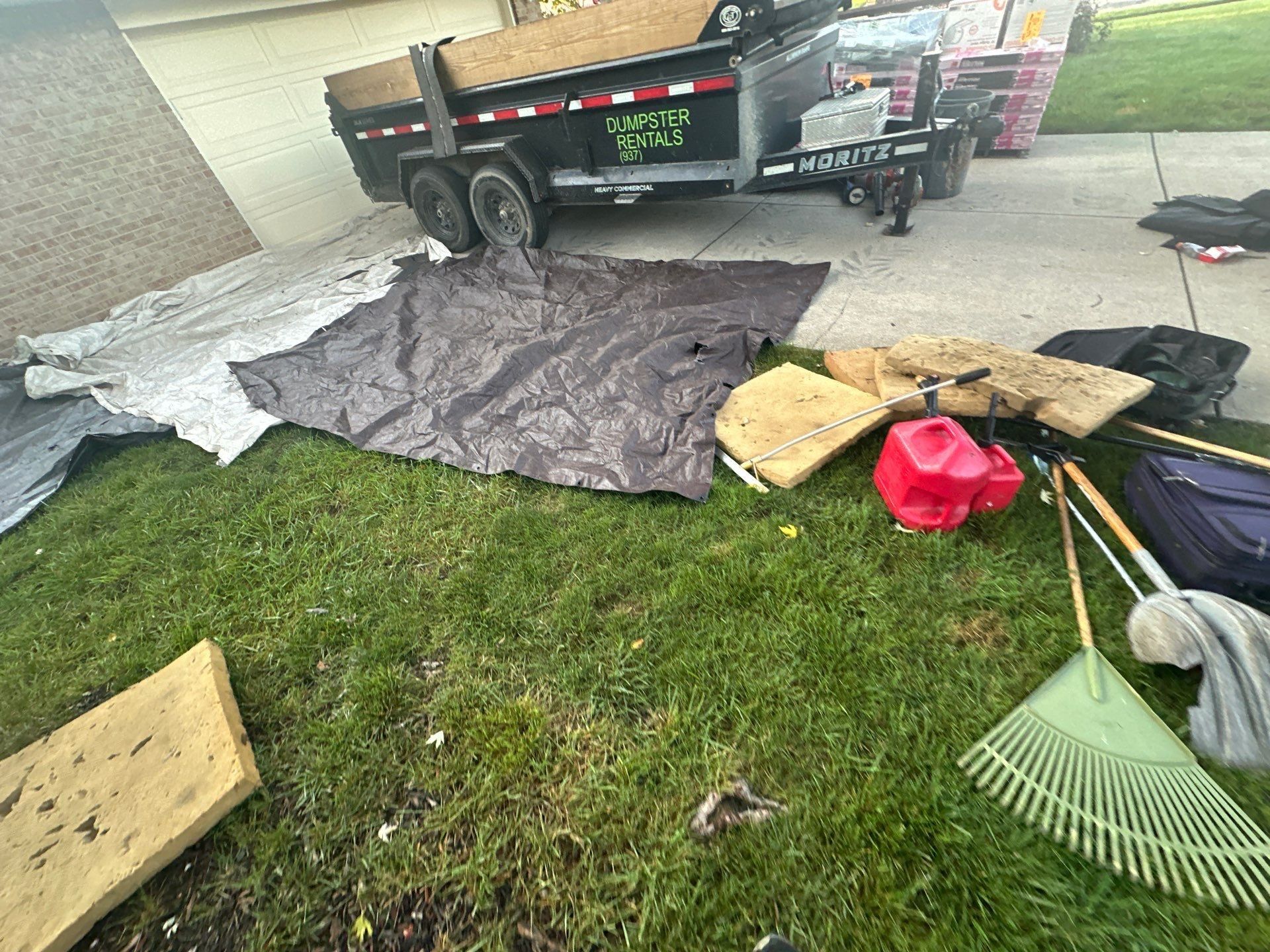 A dumpster trailer on the driveway, with tarps spread on the lawn and tools set out, Dayton, Ohio.