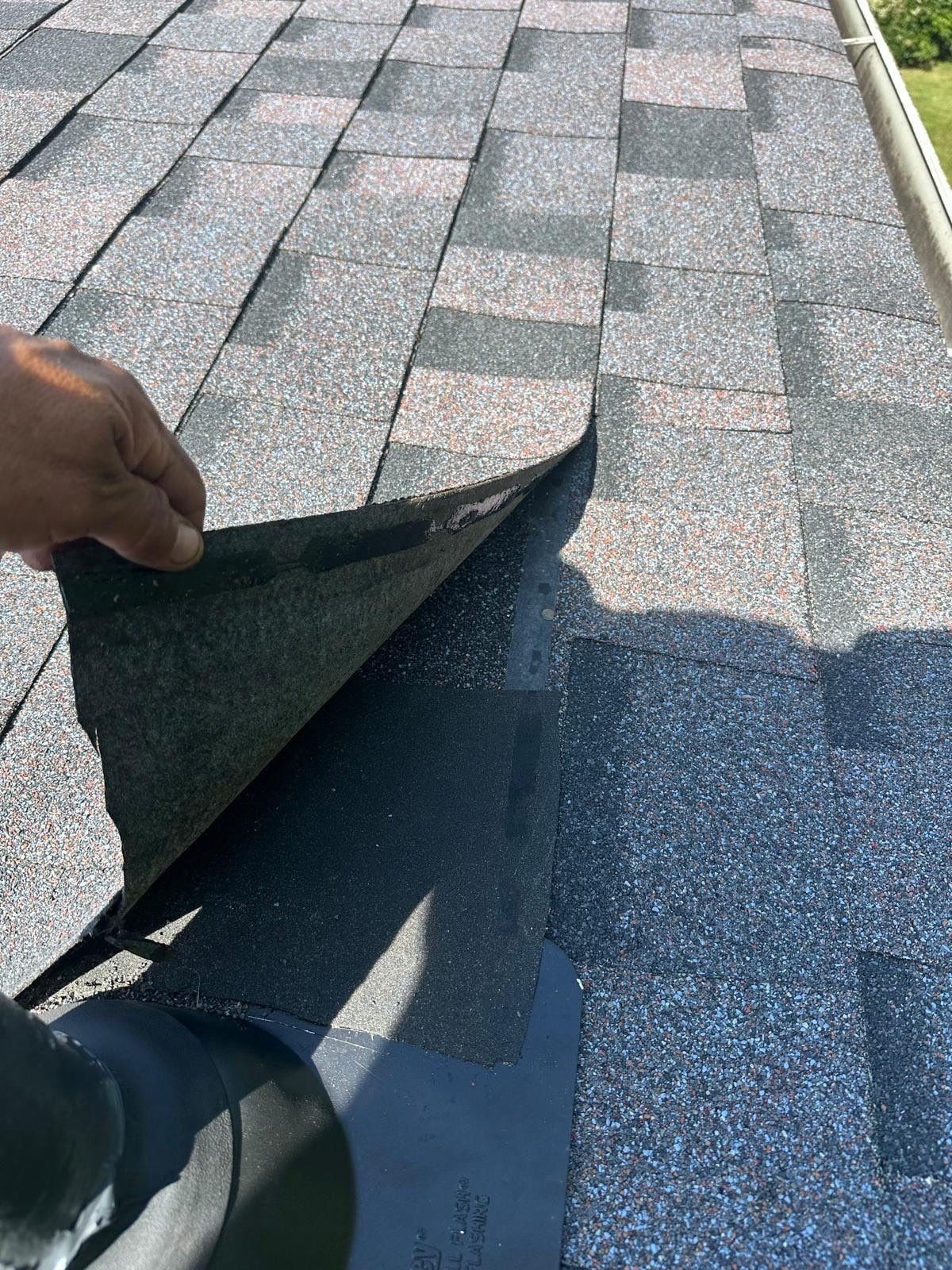 A hand lifting the edge of a new shingle on the finished roof, Beavercreek, Ohio.