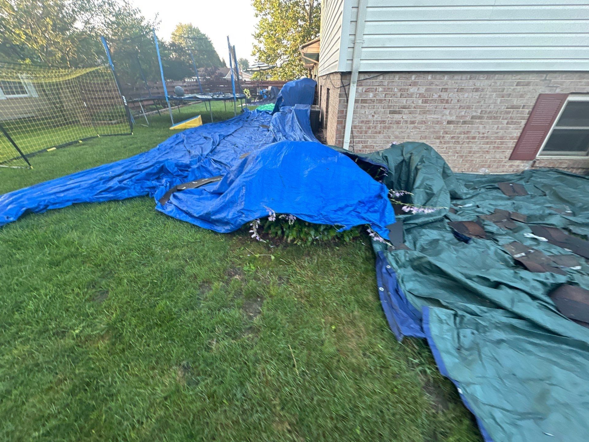 Blue and green tarps running along the back of the house toward the trampoline, Dayton, Ohio.