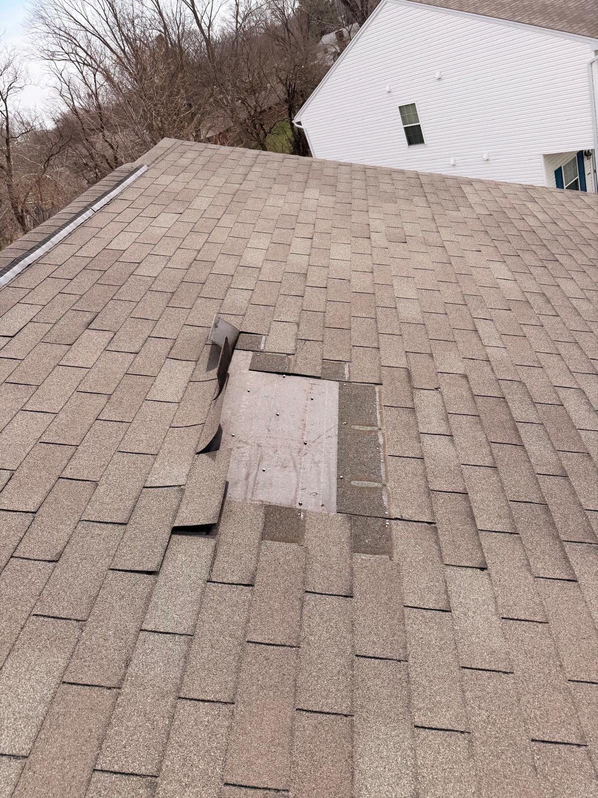 A patch of shingles gone from the middle of the slope, the underlayment showing through and the surrounding tabs folded back.