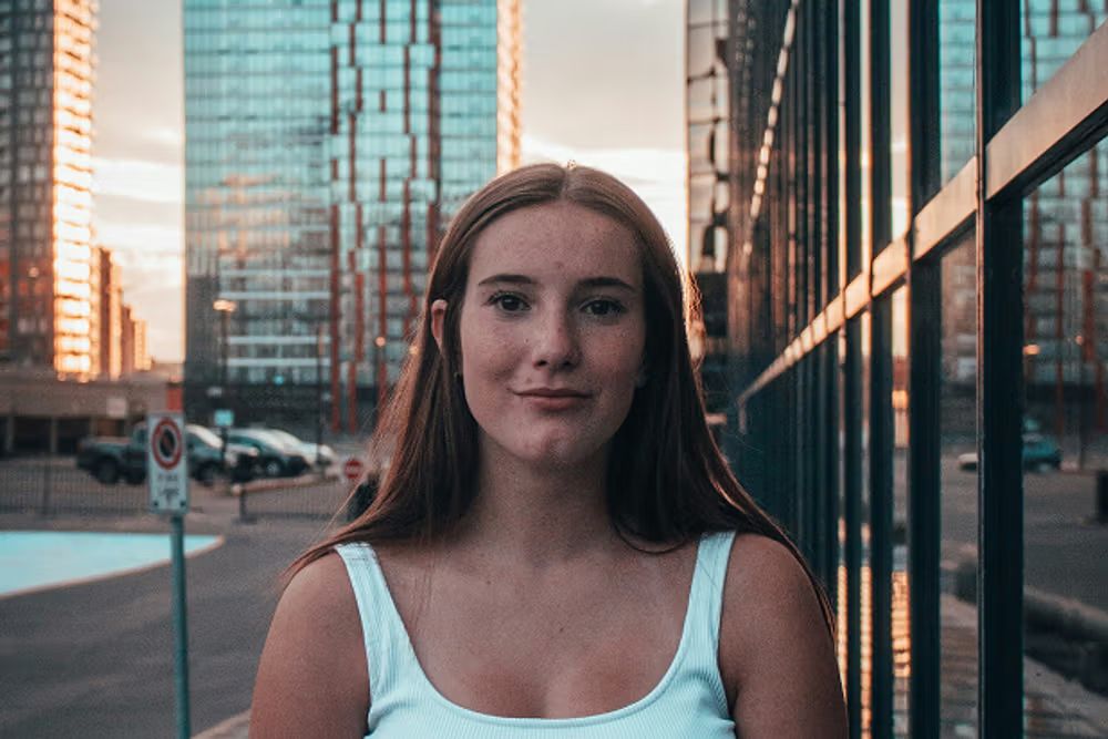 A portrait of a woman smiling against a bright, sun-drenched city backdrop.