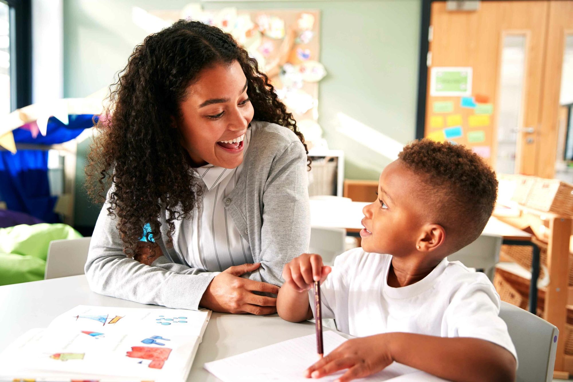 A mother showing her young son how to color with crayons in a bright.