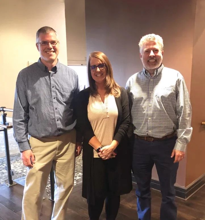 A portrait of three Bridgeway team members smiling together in a modern workspace.