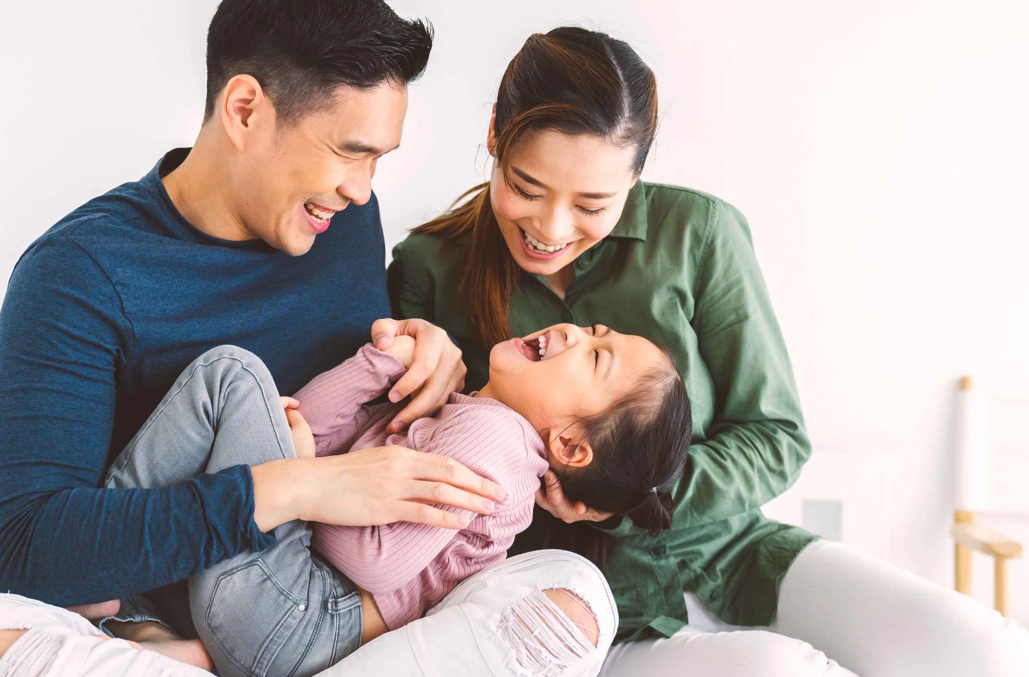 A happy family of three laughing and enjoying time together in a bright, indoor setting.
