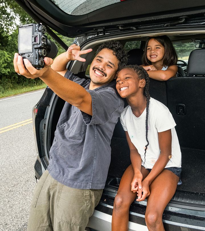 A smiling family taking a selfie together at the back of a parked car.