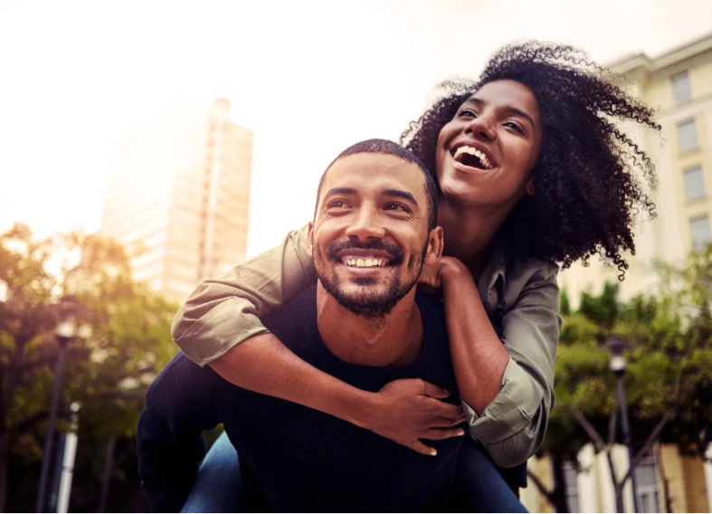 A man giving his girlfriend a piggyback ride while they both smile.