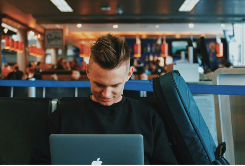 A man using a laptop in an airport terminal seating area.