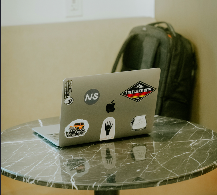 A laptop with a sticker-covered lid sitting on a table.