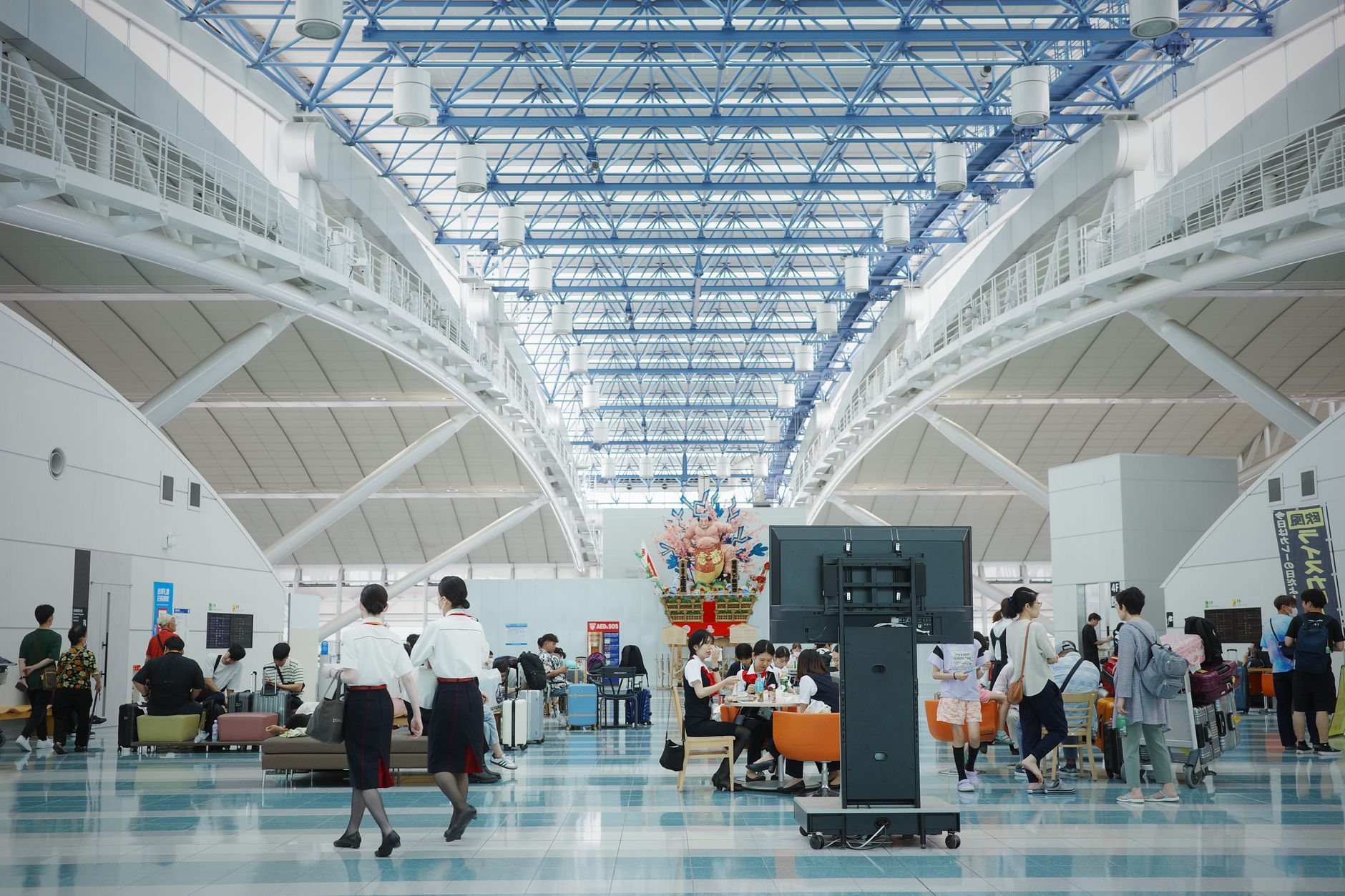 Travellers walking through the bright arrivals hall of a Japanese airport toward immigration and customs.
