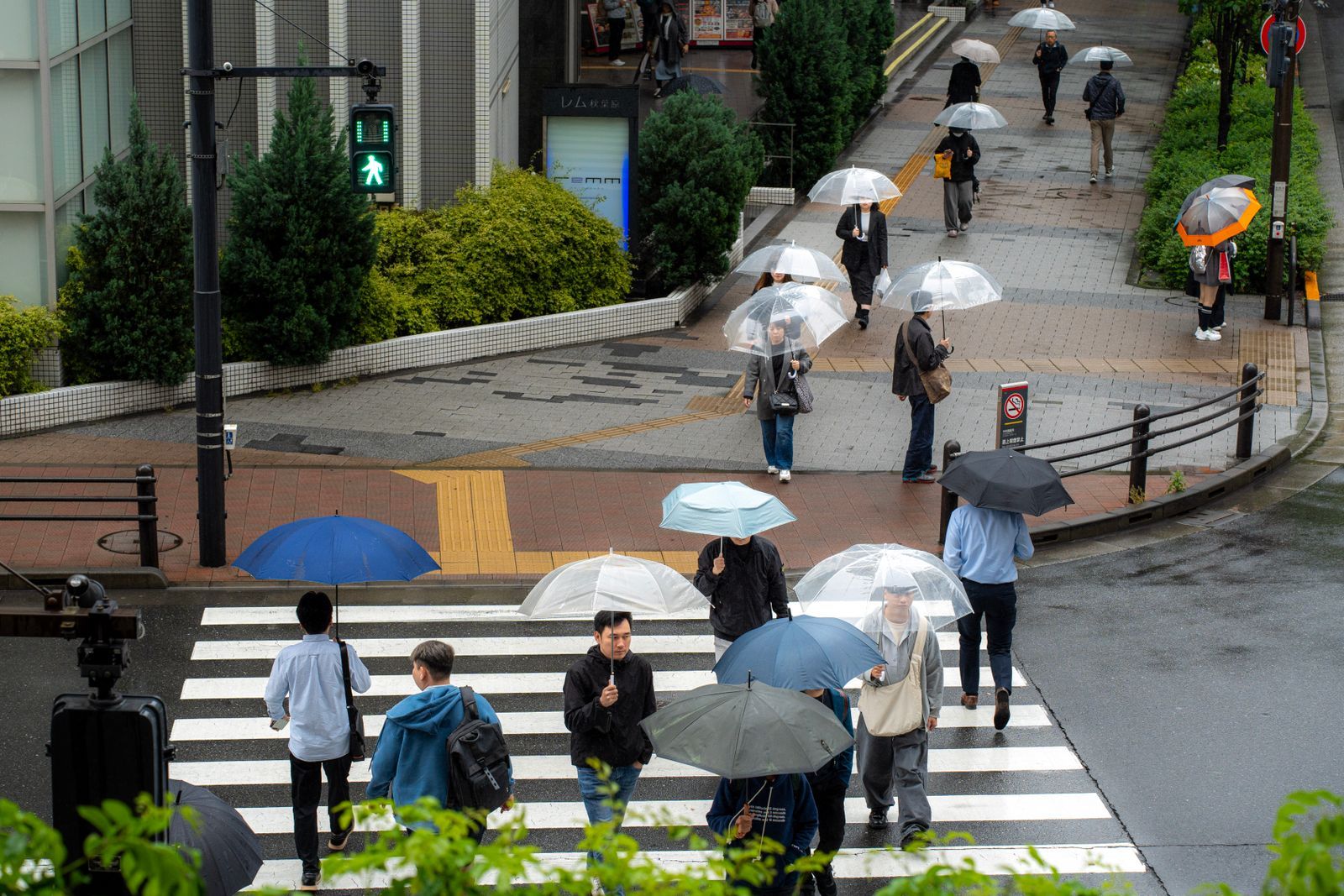 People crossing a Tokyo street with umbrellas during heavy rain on an overcast late-summer day