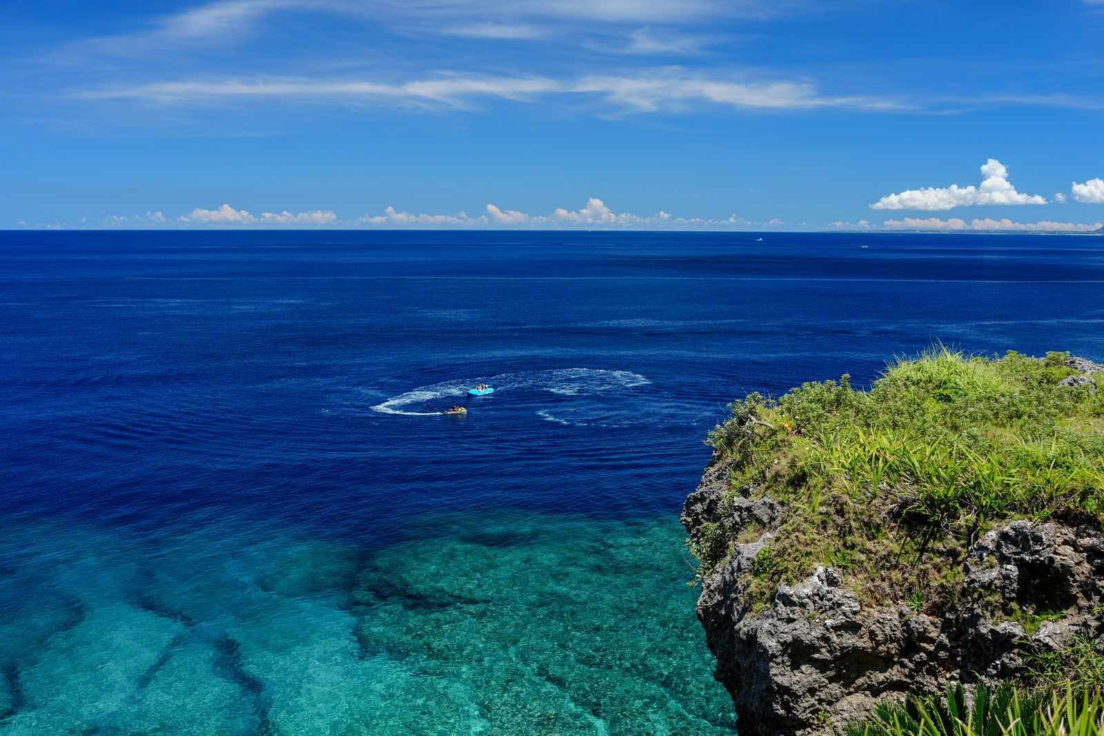 Crystal-clear turquoise sea below a rocky cliff under blue sky in Okinawa, Japan