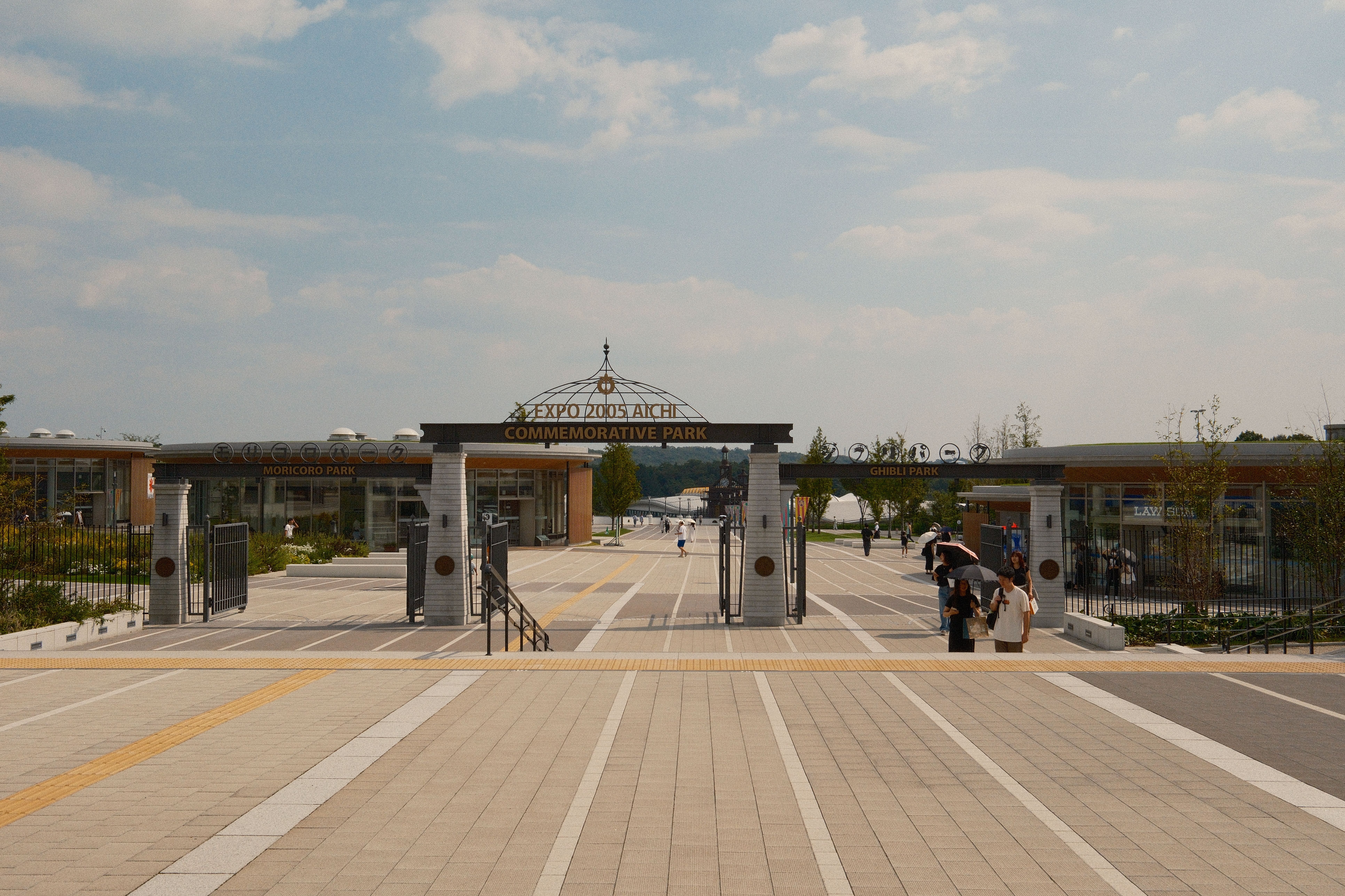 Visitors walking and cycling on the wide entrance path of Expo 2005 Aichi Commemorative Park, home of Ghibli Park