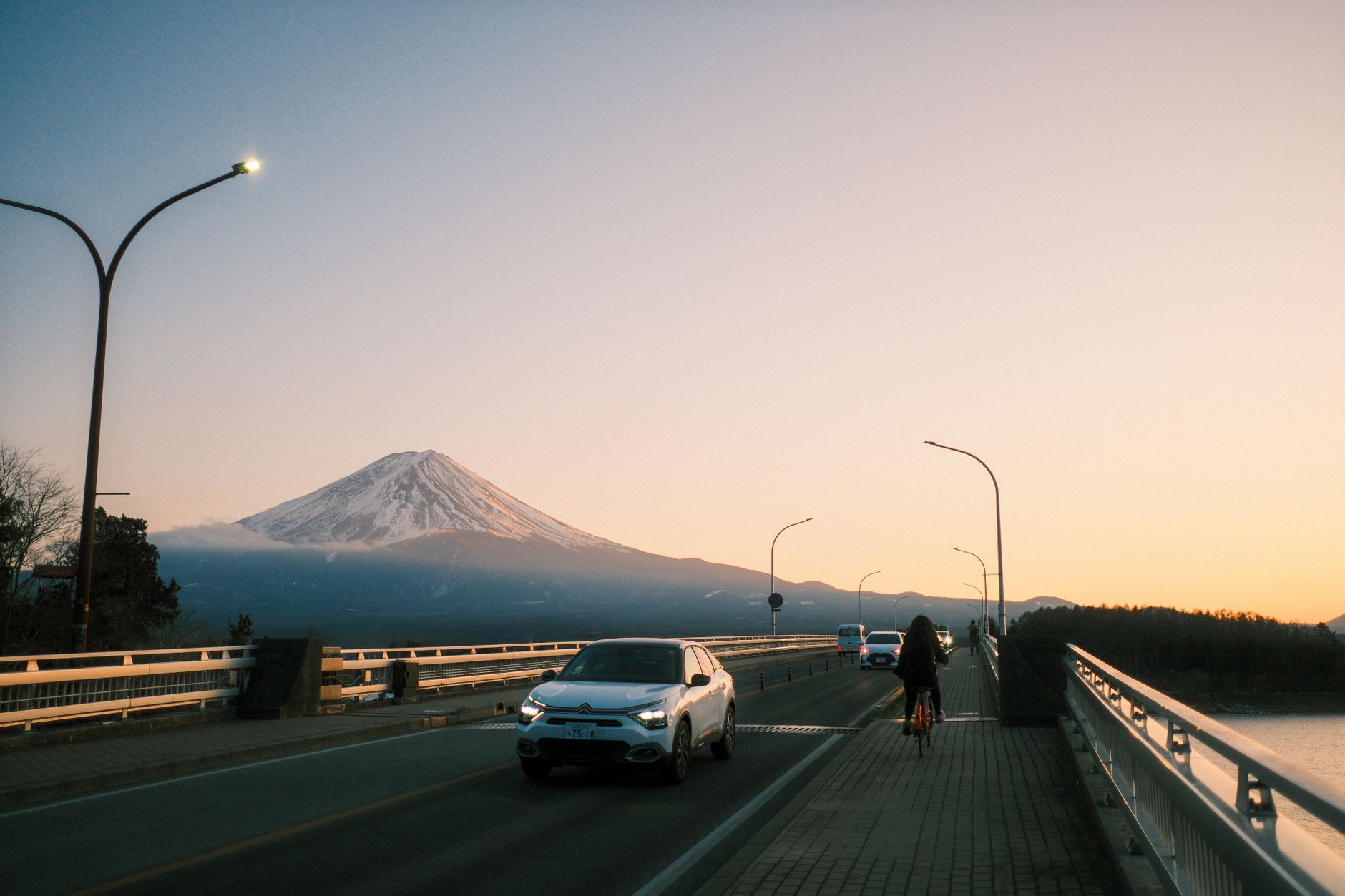Cars driving on a bridge at sunset with Mount Fuji rising in the background at Fujikawaguchiko, Japan