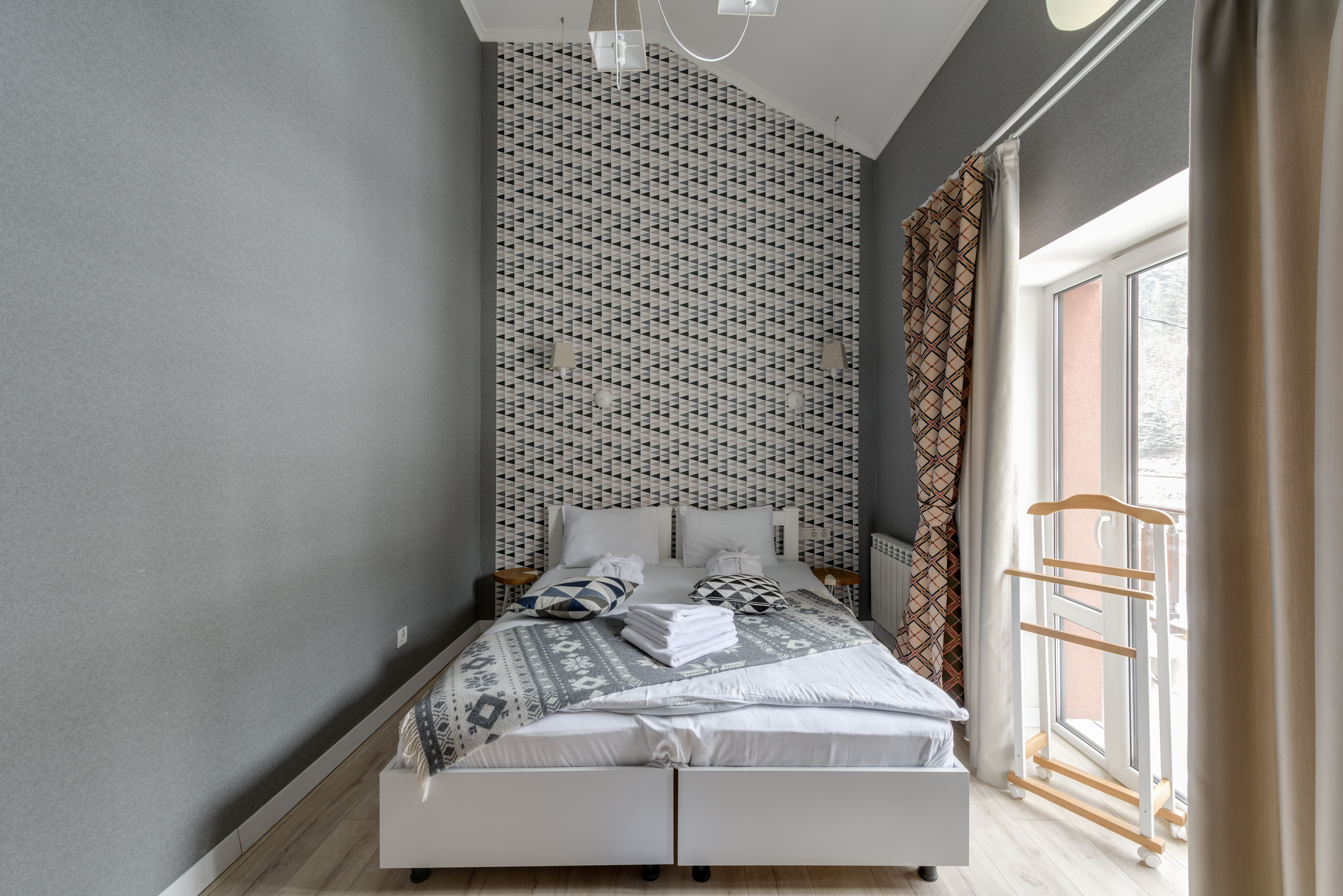 Modern hotel room with a neatly made double bed, soft lighting and natural daylight from the window