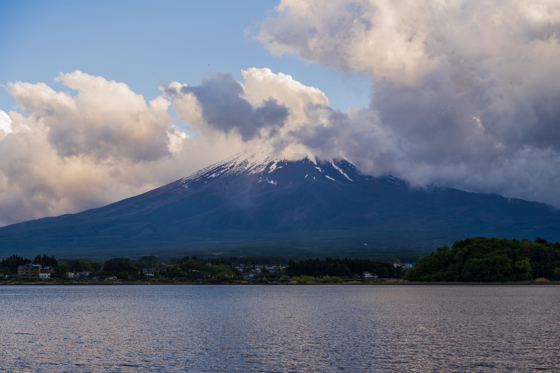 Mount Fuji under broken cloud seen across the water from Lake Kawaguchi in Yamanashi, Japan