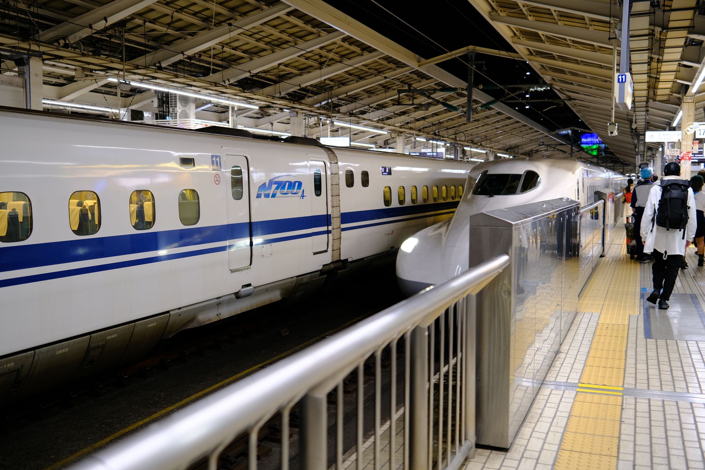 Passengers with luggage boarding a Shinkansen bullet train at a busy Tokyo station platform