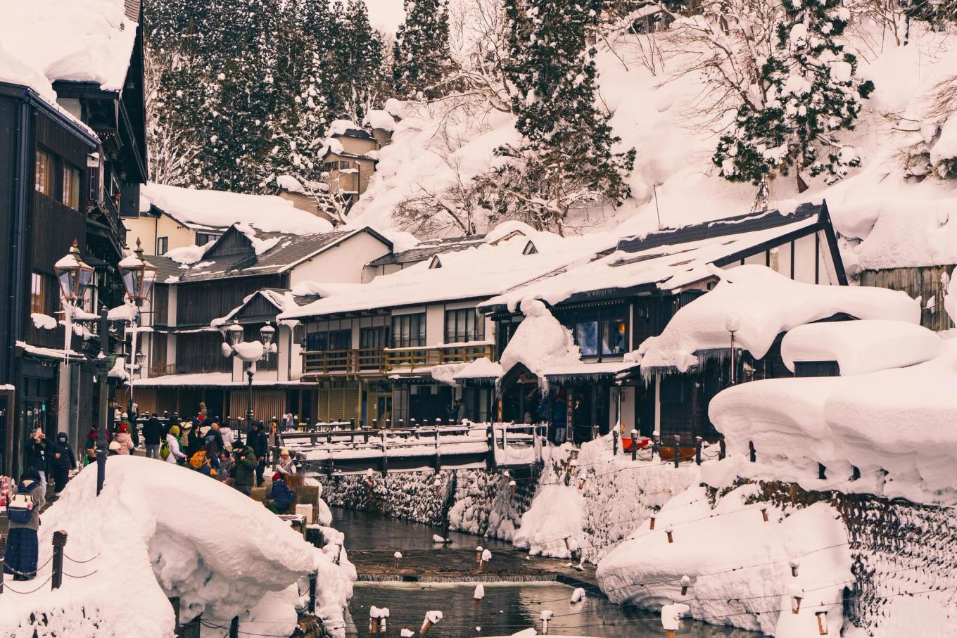 Day visitors on the snowy riverside street of Ginzan Onsen, with deep snow on roofs and railings