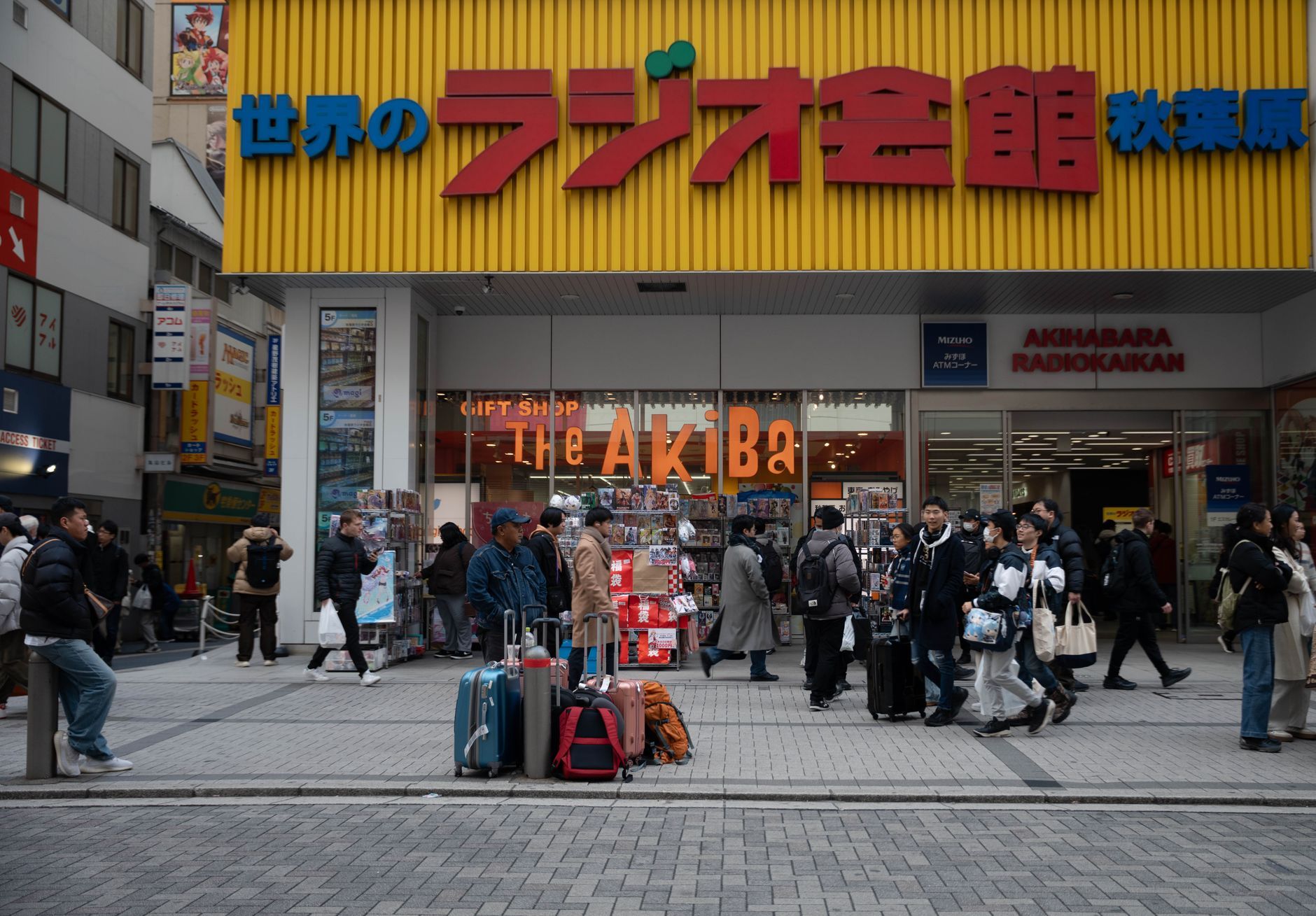 Shoppers carrying suitcases and paper bags outside a busy electronics store in Akihabara, Tokyo.