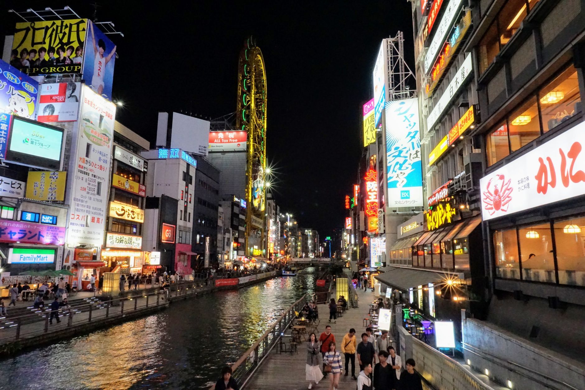 Nighttime view of the Dotonbori canal in Osaka, crowded with people under bright neon signs and reflections on the water