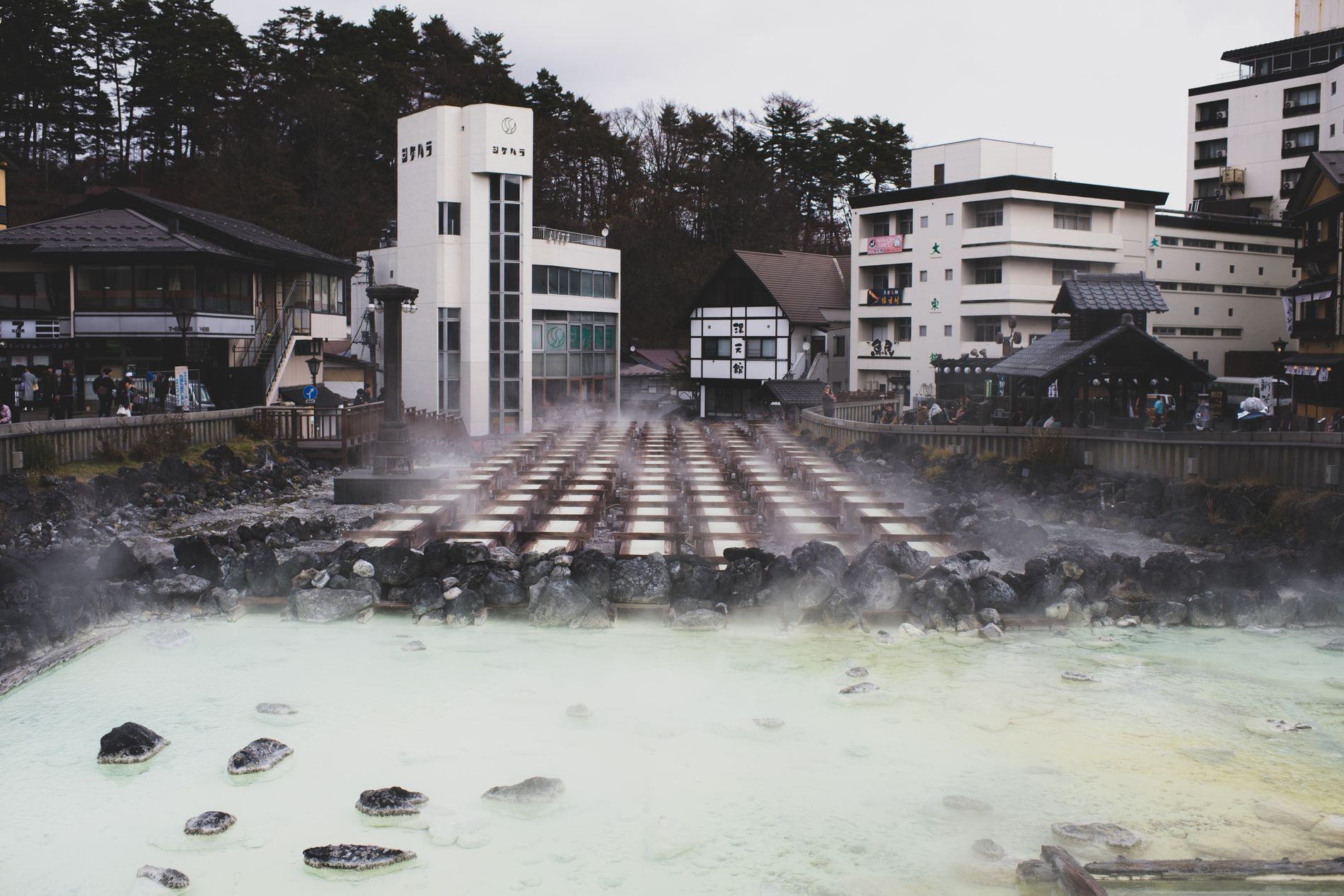 Steam rising from the pale green sulphur pool and wooden cooling channels at the heart of a Japanese onsen town