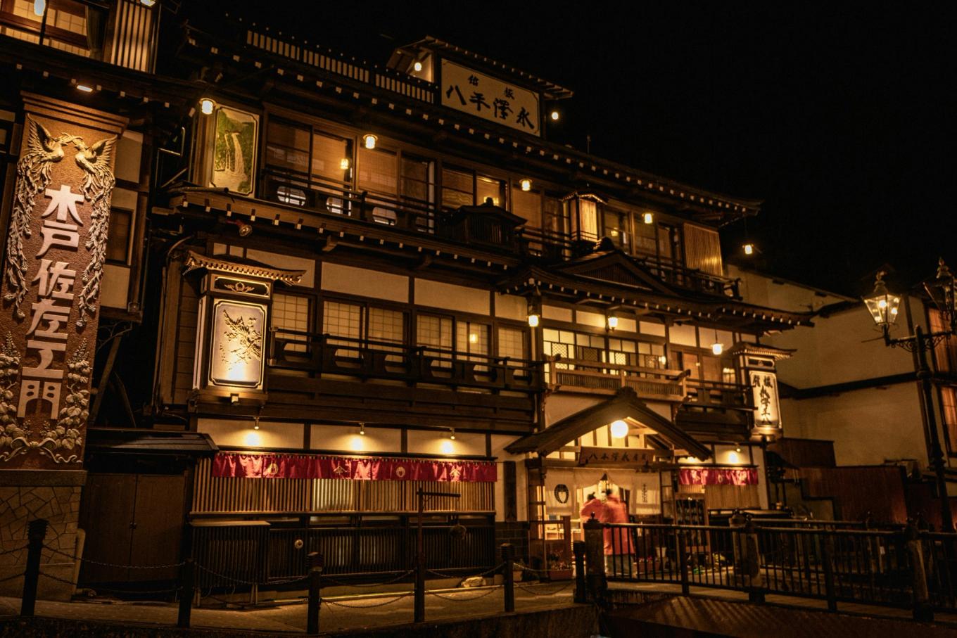 Ryokan Nagasawa Heihachi in Ginzan Onsen lit up at night, its wooden facade and carved signboards glowing