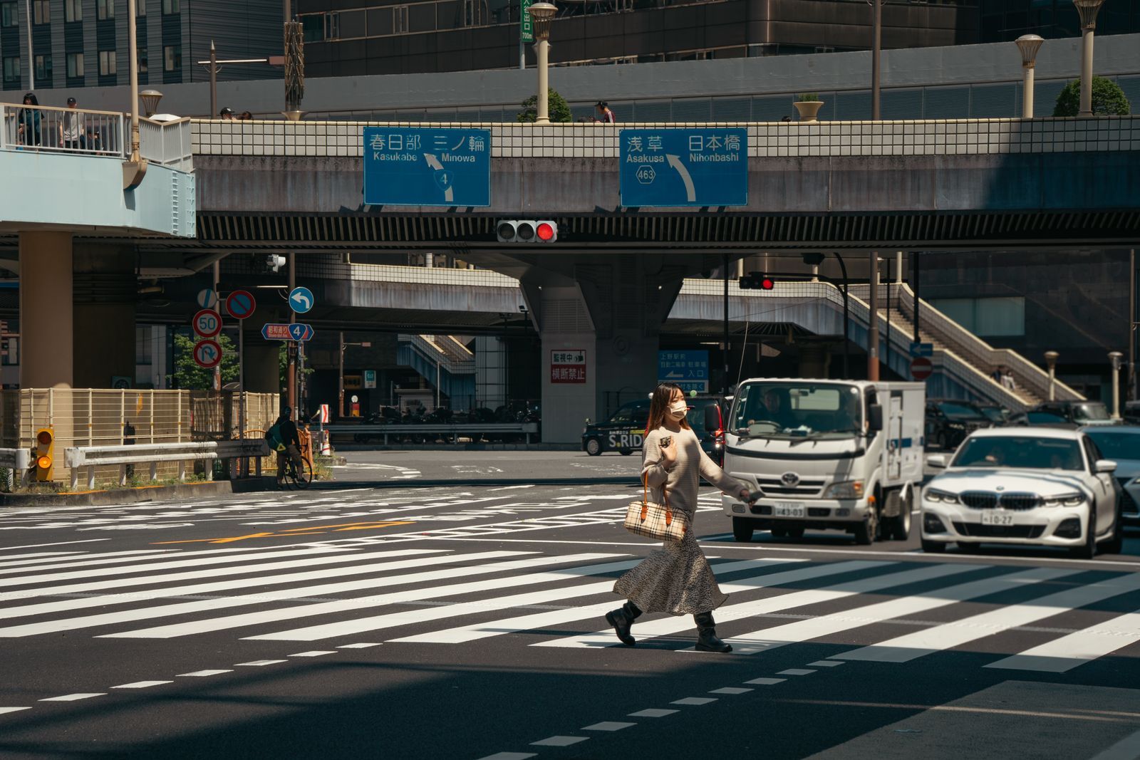 A woman crossing a busy Tokyo intersection alone in daylight, with city traffic behind her