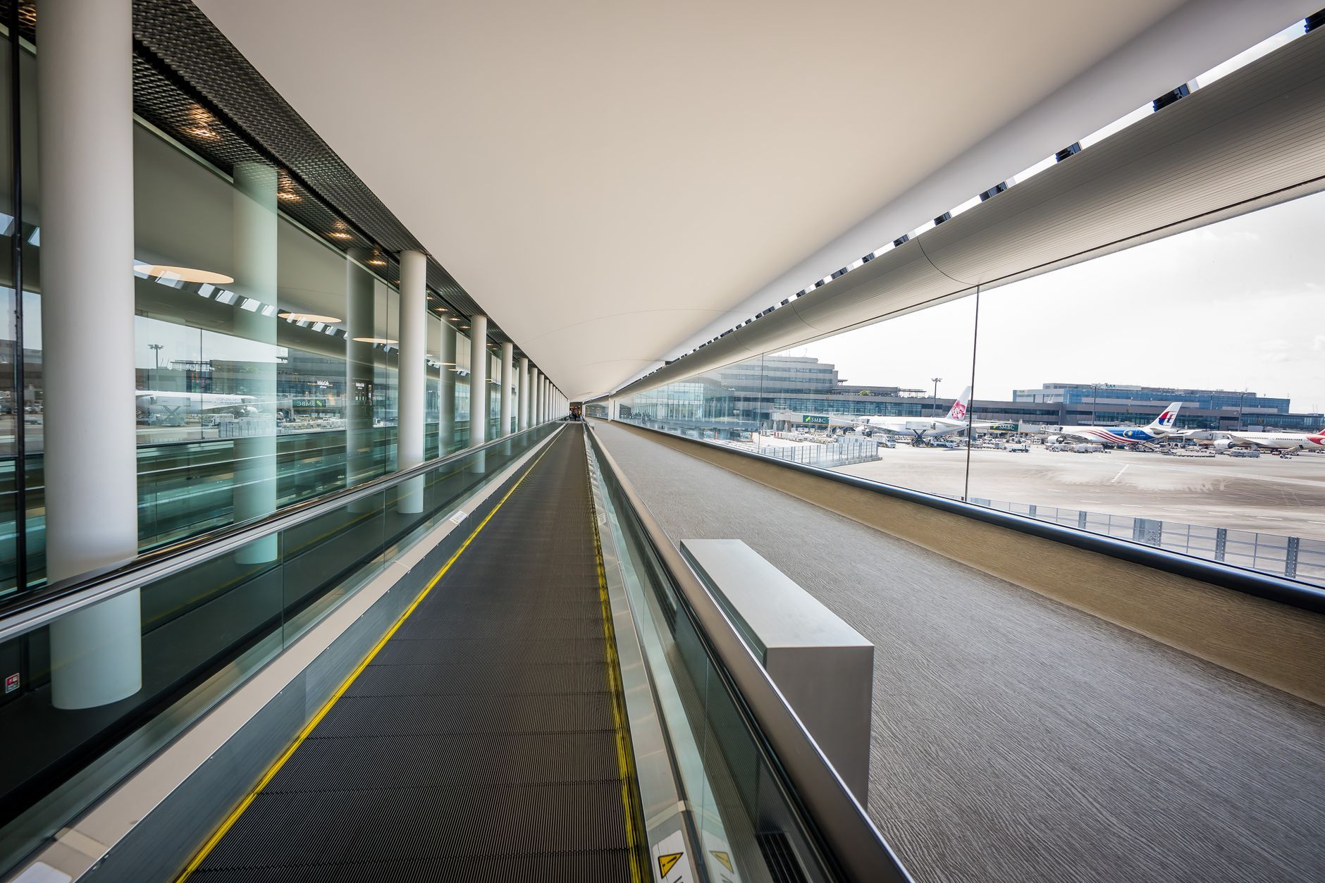 Interior of a modern Japanese airport terminal with a moving walkway and planes outside the window.