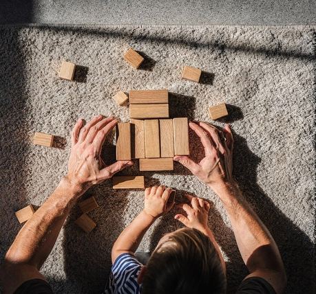 Un adulto e un bambino costruiscono con blocchi di legno su un tappeto, visti dall’alto.