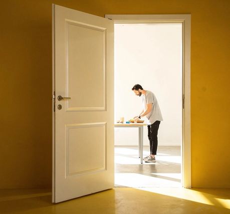 Una porta socchiusa su una stanza luminosa e vuota.