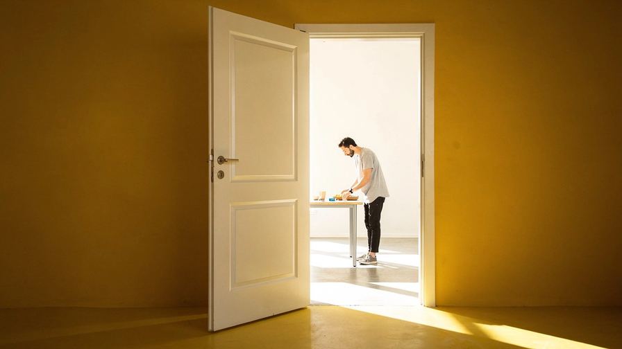 Una porta socchiusa su una stanza luminosa e vuota.
