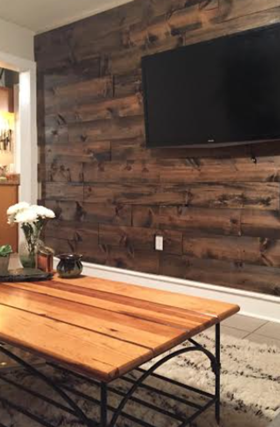 Living room with stained wood accent wall, mounted TV, and rustic coffee table