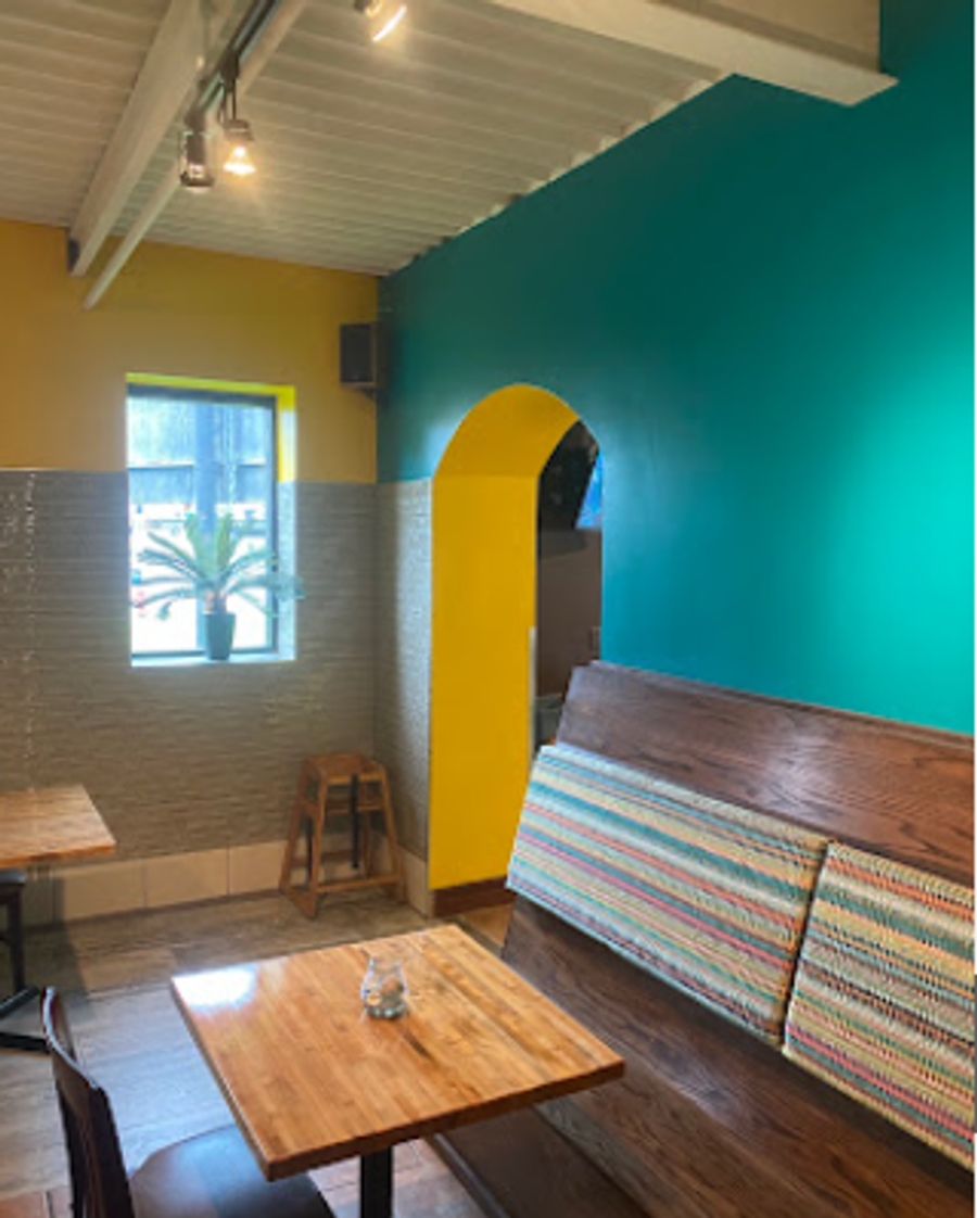 Restaurant interior with bold teal and yellow walls, yellow archway, and wooden bench seating