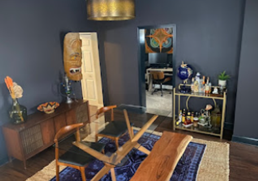 Dining room with deep navy walls, brass pendant light, mid-century furniture, and bar cart