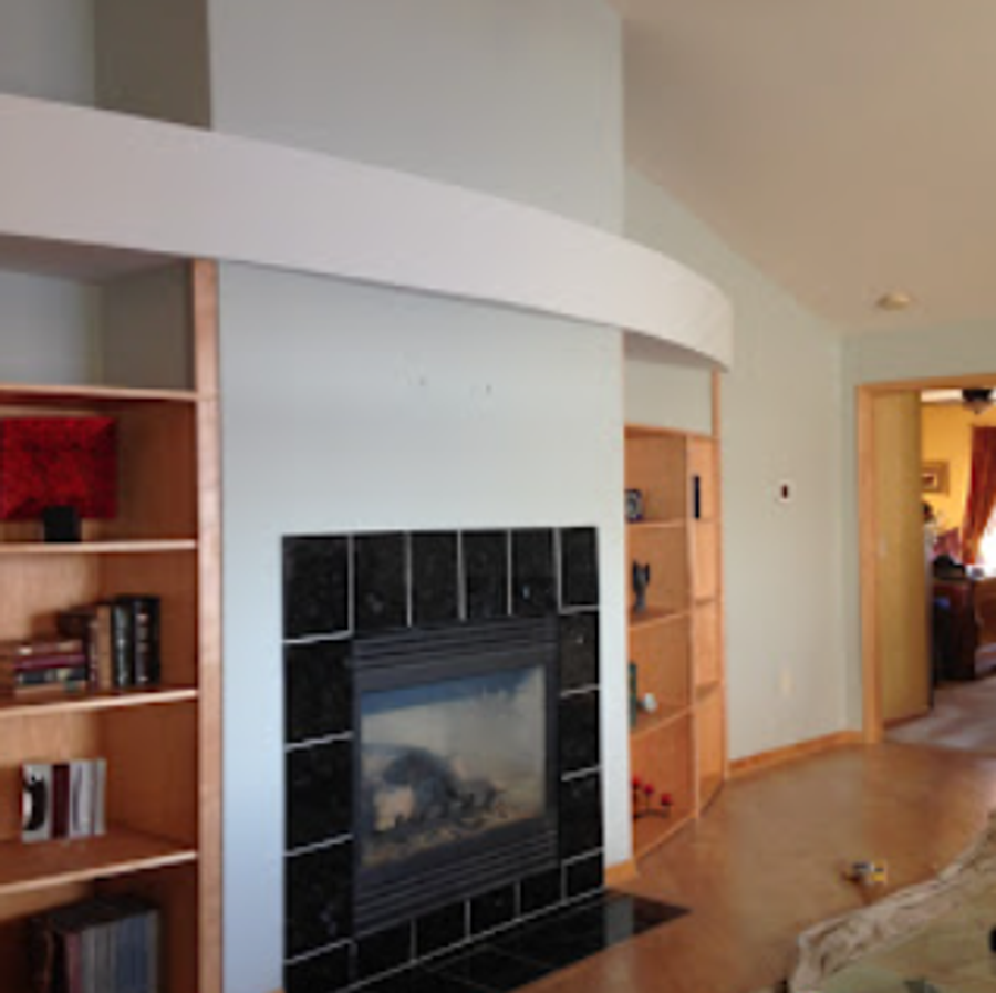 Living room with curved white accent wall, dark tiled gas fireplace, and warm-wood built-in bookshelves