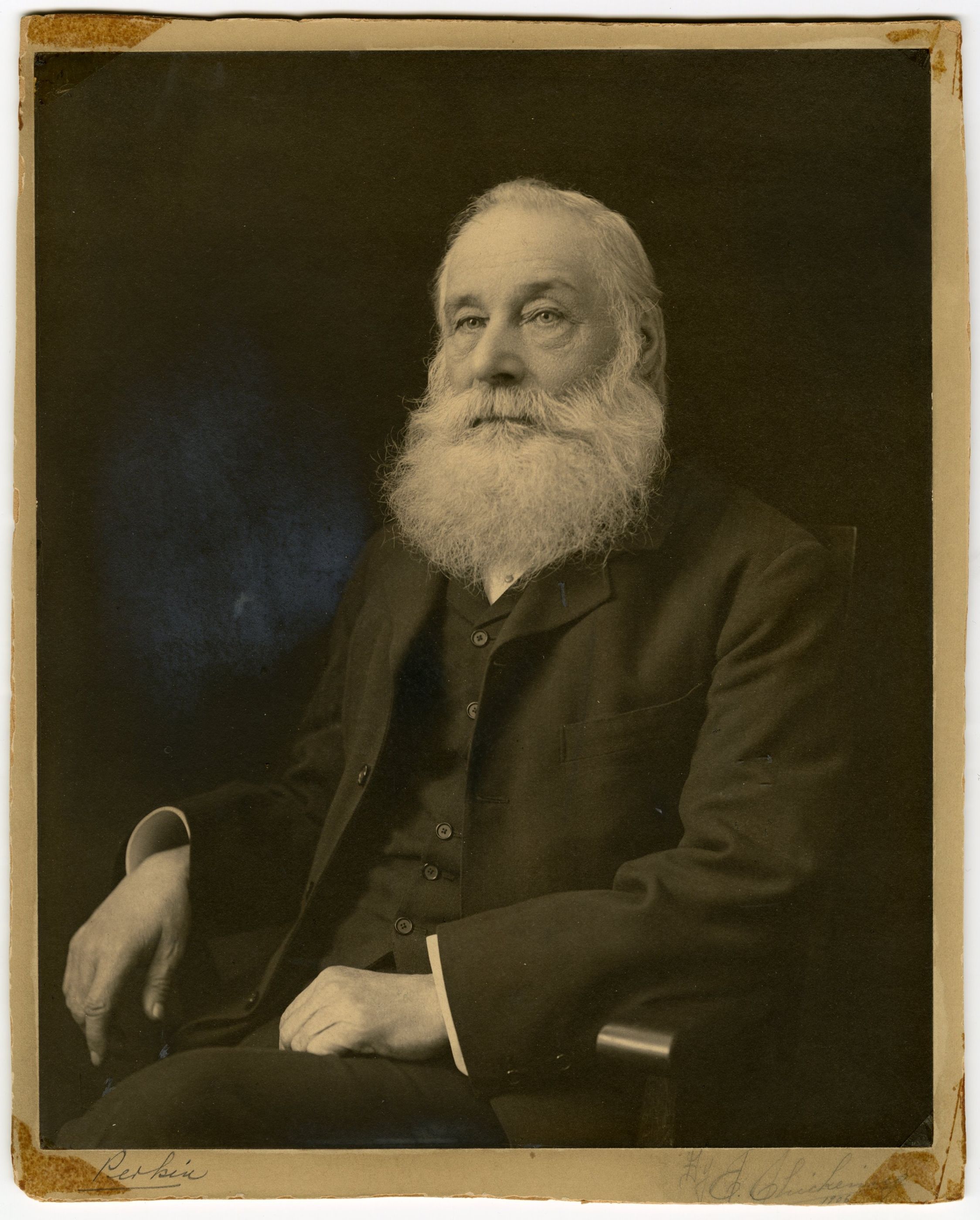 William Henry Perkin seated, with a long white beard and both hands resting on his lap and chair