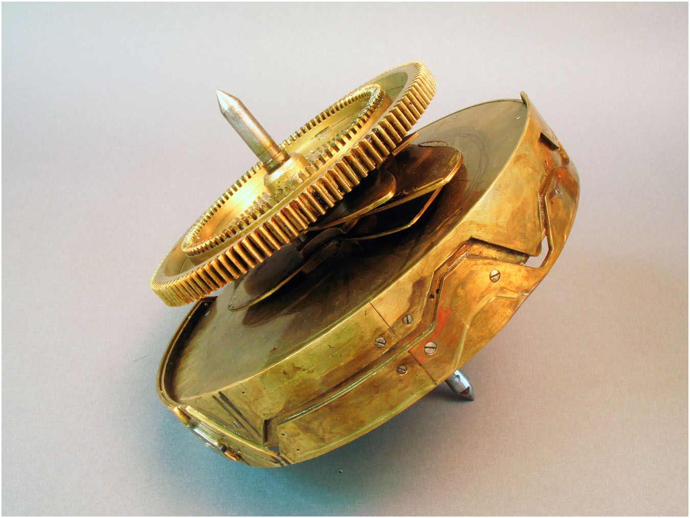 A brass cam drum and gear wheel, with shaped tracks screwed around its edge.