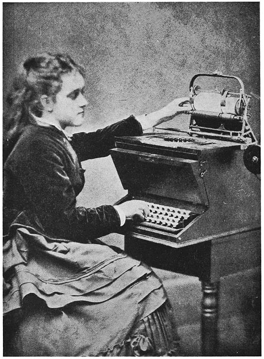 Lillian Sholes seated at a writing machine with one hand near the keyboard and the other lifting the paper carriage