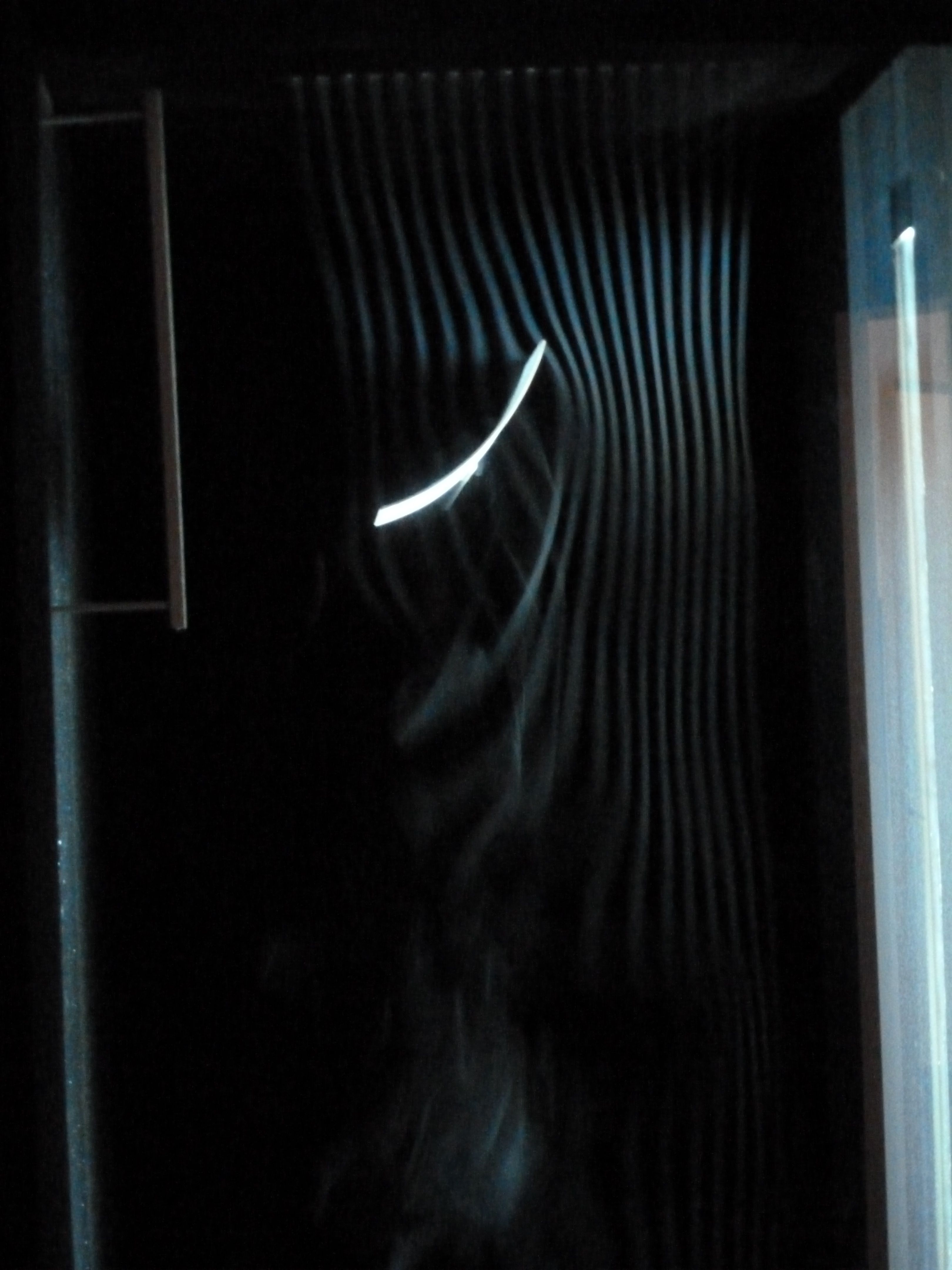 Pale smoke threads bend around a bright curved surface inside a dark modern reconstruction of Marey's chamber.
