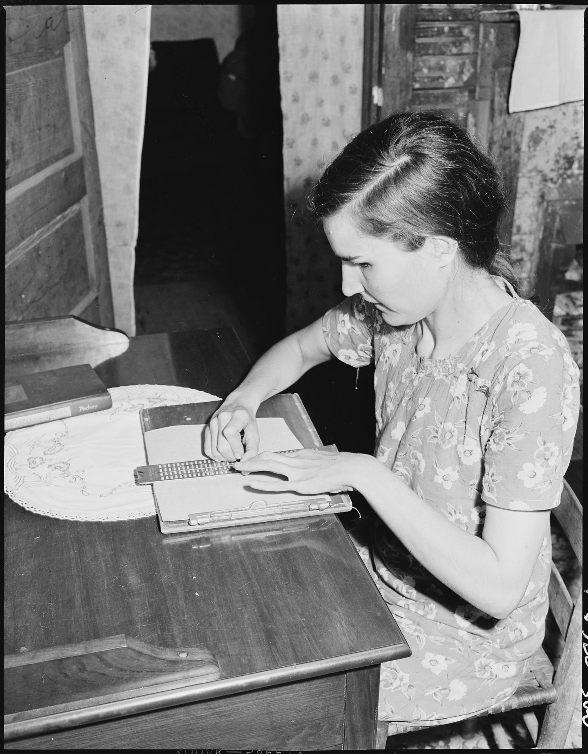 Lucy Sergent seated at a table, holding a stylus over a writing guide while her other hand rests on the paper
