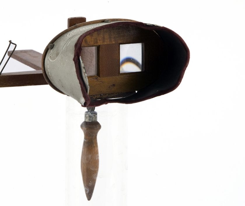 The hood, paired lenses and wooden handle of a handheld stereoscope