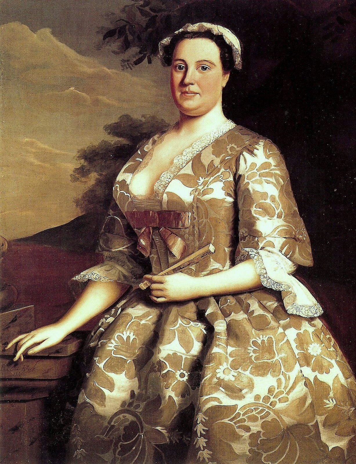 Anne Shippen Willing standing in a flower-patterned silk gown with lace at her neckline and sleeves, holding a closed fan beside a stone pedestal