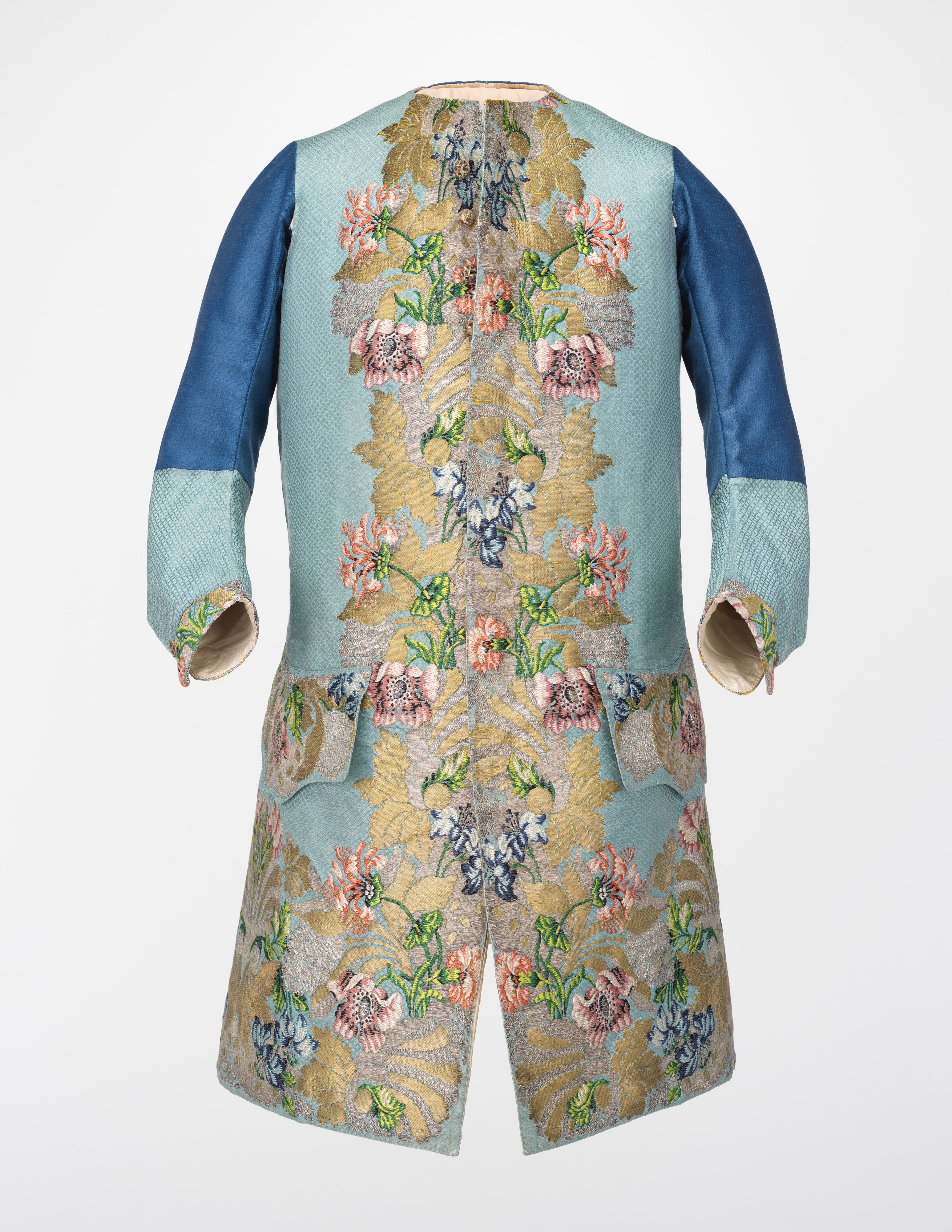 A long pale-blue sleeved waistcoat with pink and blue flowers and gold-coloured leaves woven around its opening, hem and pockets