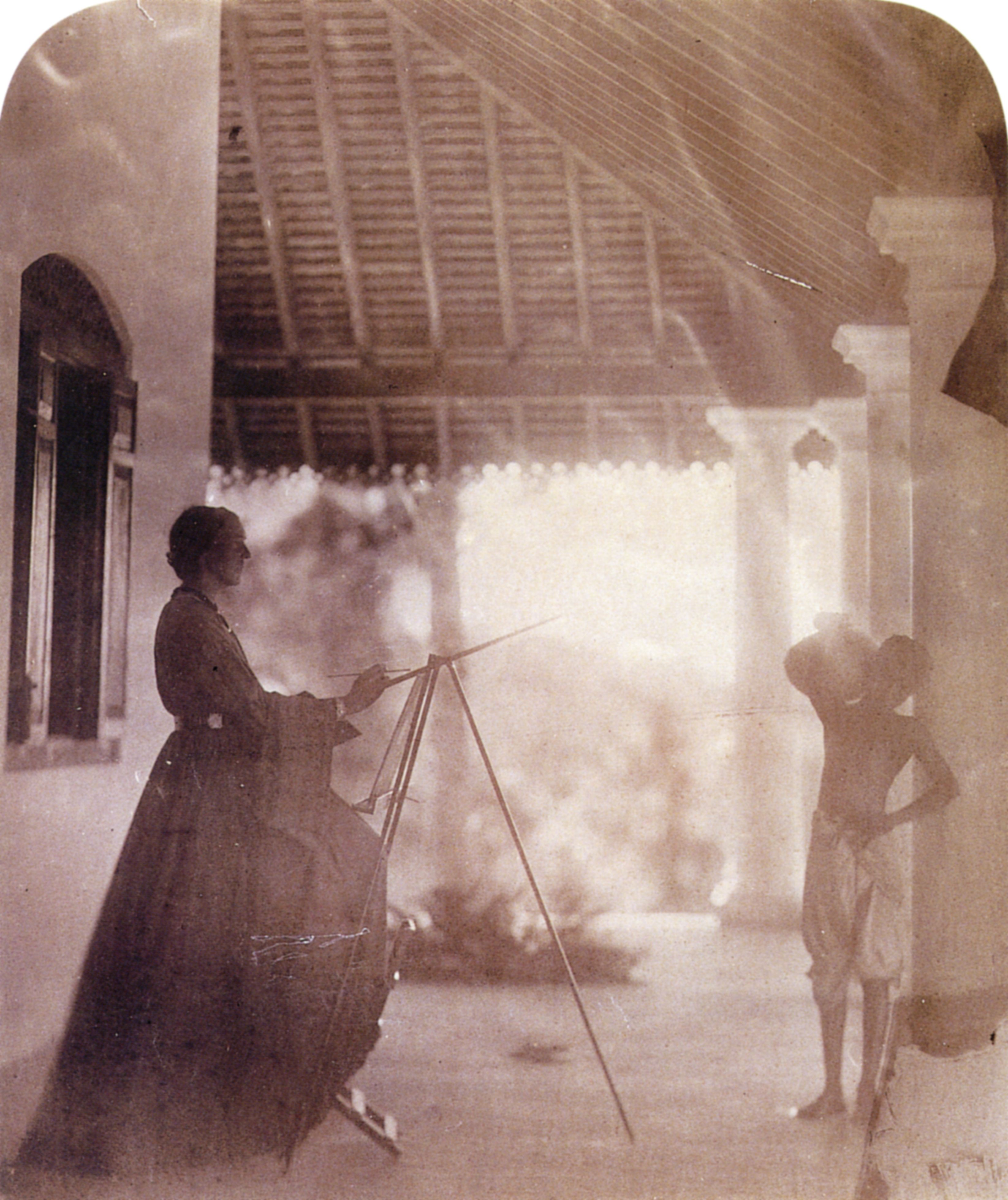 Marianne North at an easel on a verandah, with a boy standing beside a column.
