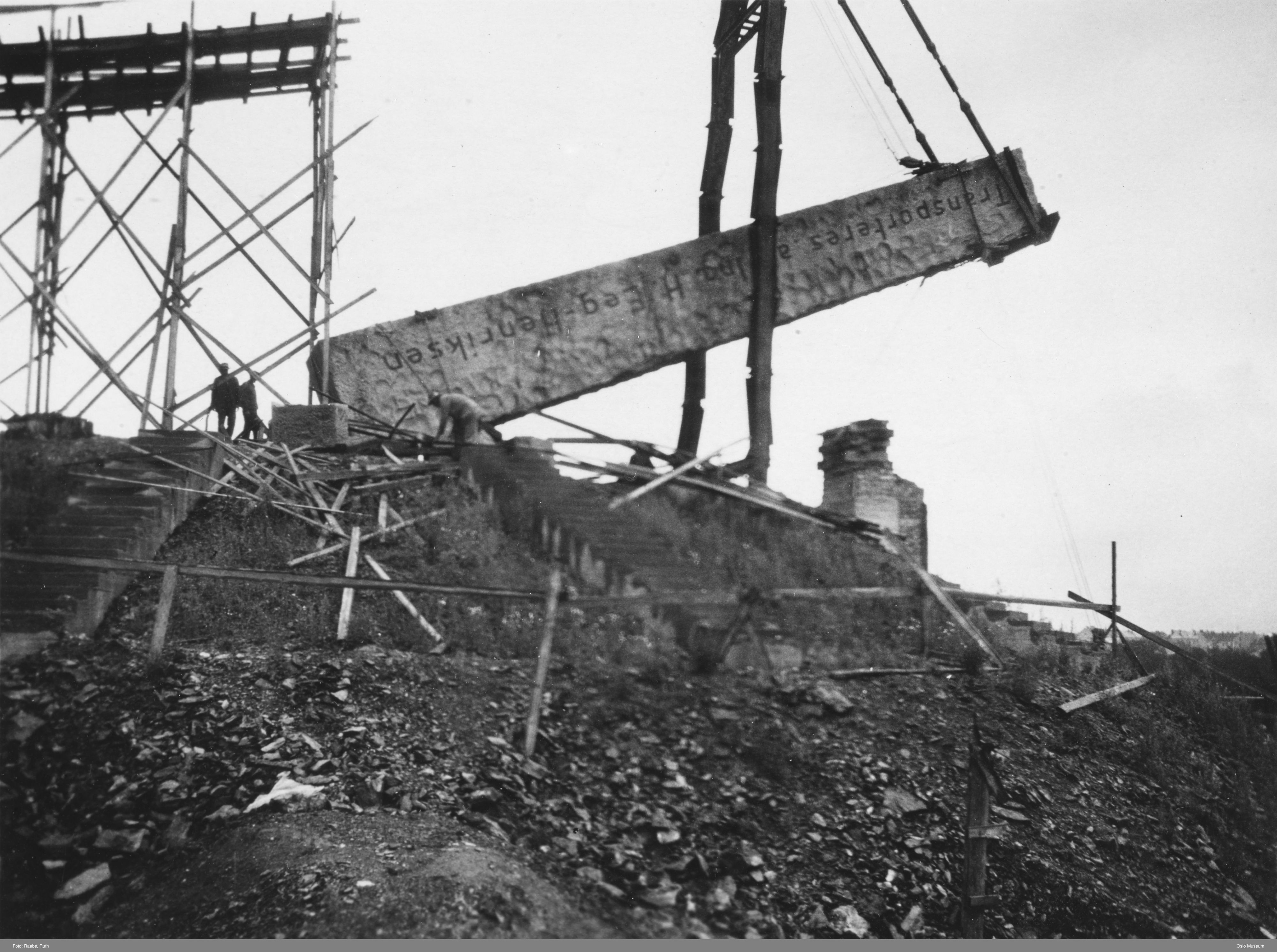 The long granite block being raised at an angle by cables and a tall lifting structure, with men beside it.